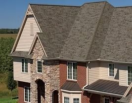 Two-story house with a stone facade, red brick, and brown shingle roof on a sunny day.