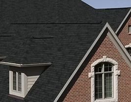 Black shingled roof on a brick house with white trim around windows.