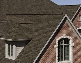 Brown shingled roof of a brick house with white-framed windows.