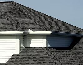 Dark asphalt shingle roof with black gutters, attached to a house with white siding.