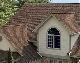 Brown shingled roof on a house with white siding and a large window.