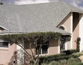 Gray-roofed house with beige stucco walls, windows, and manicured bushes in front.
