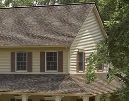 Two-story house with brown shingle roof, tan siding, and brown shutters.