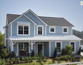 Two-story blue farmhouse with white trim, porch, and a dark gray roof against a clear sky.