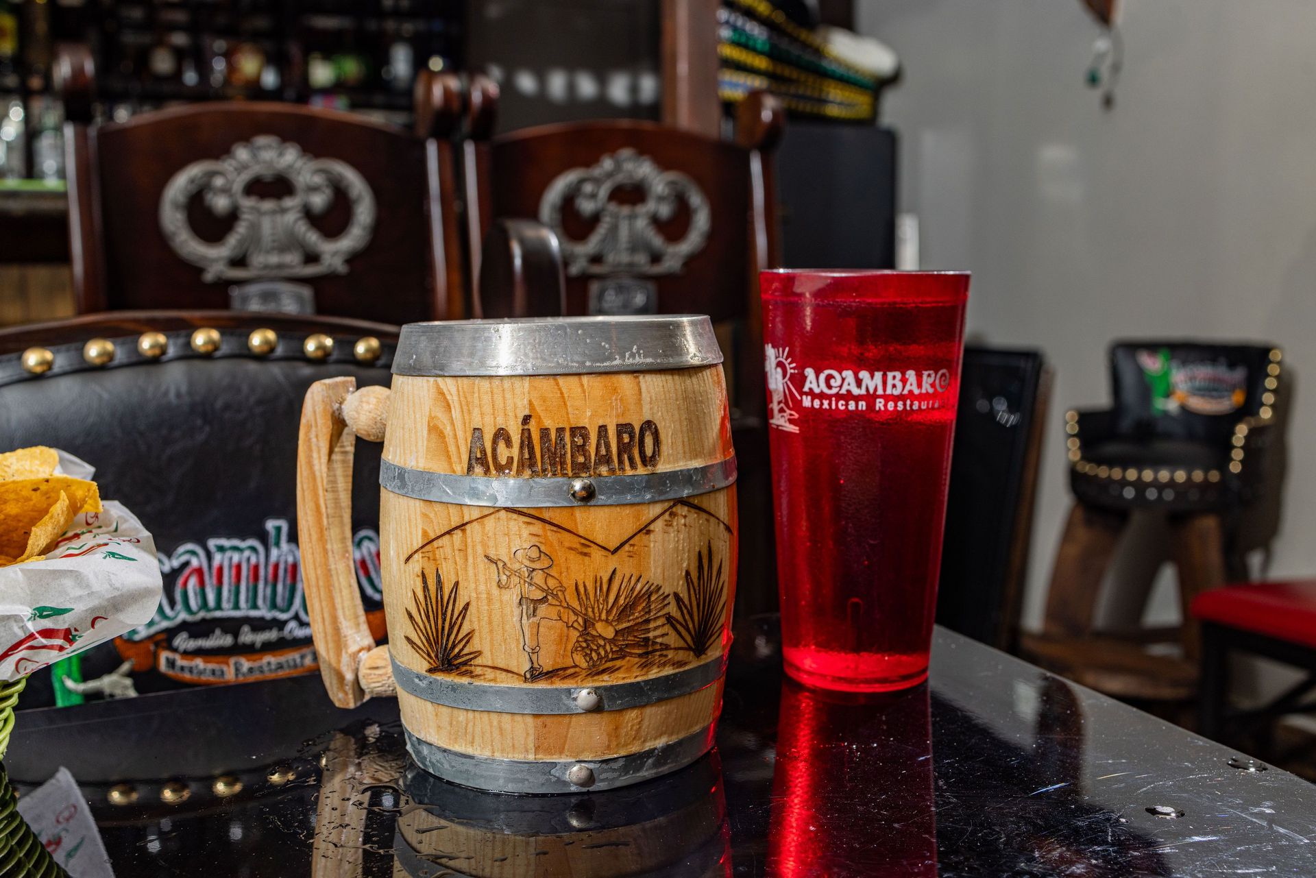 Wooden mug and red plastic cup on a bar with chairs in the background.