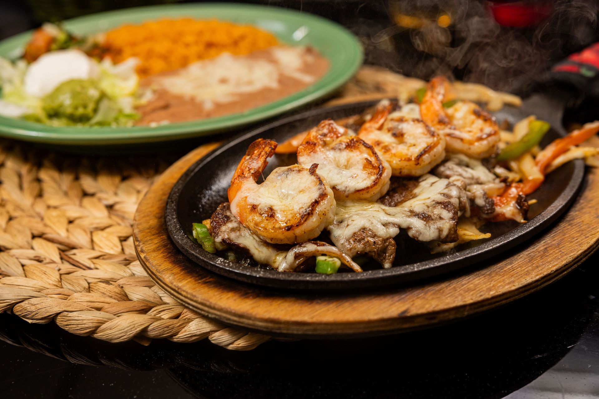 Sizzling shrimp fajitas with cheese and a plate of rice, beans, and guacamole.