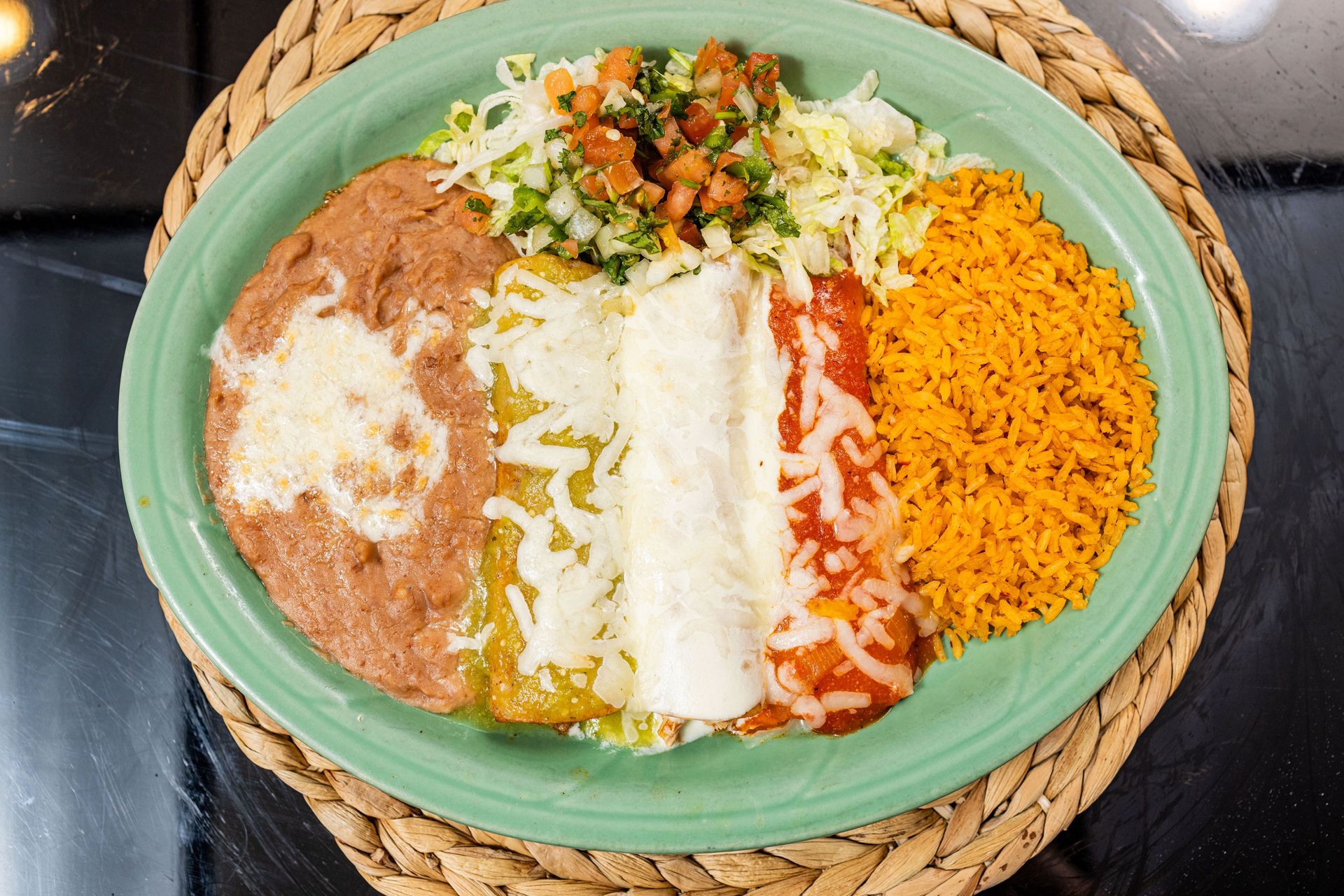 Plate of Mexican food: refried beans, enchiladas with cheese and sauce, rice, and pico de gallo.