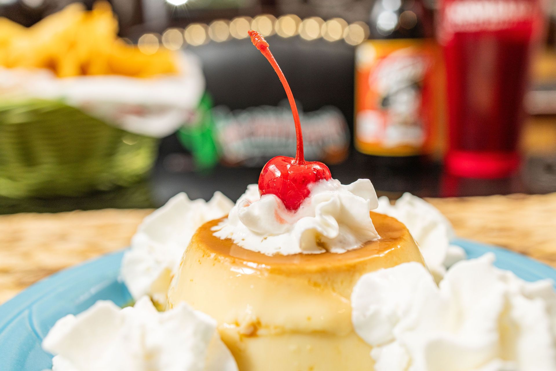 Flan dessert topped with whipped cream and cherry, on a blue plate.