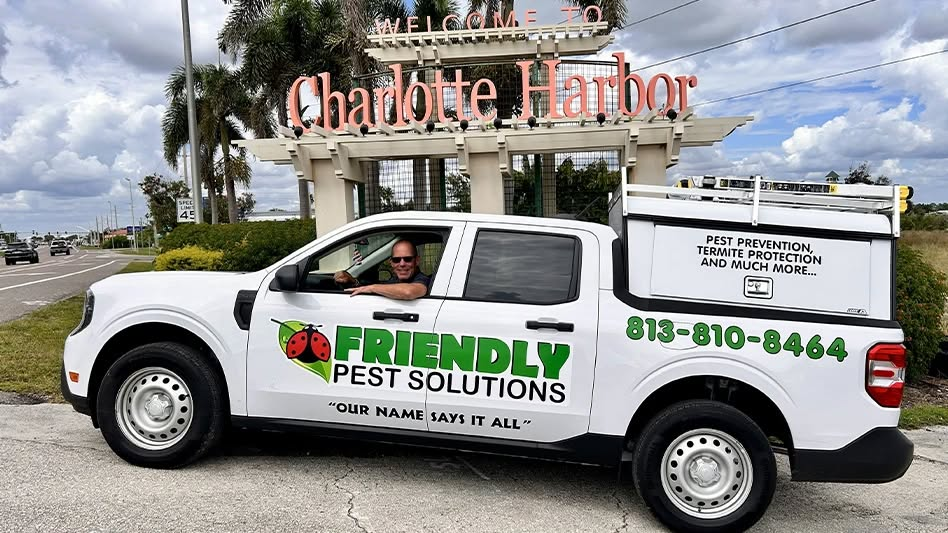 A Friendly Pest Solutions work truck parked in front of a Charlotte Harbor sign with a driver visible in the window.