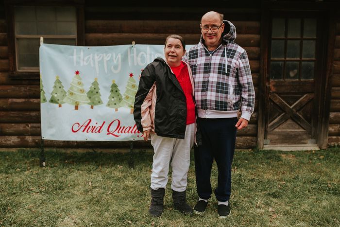 A man and a woman are posing for a picture in front of a log cabin.
