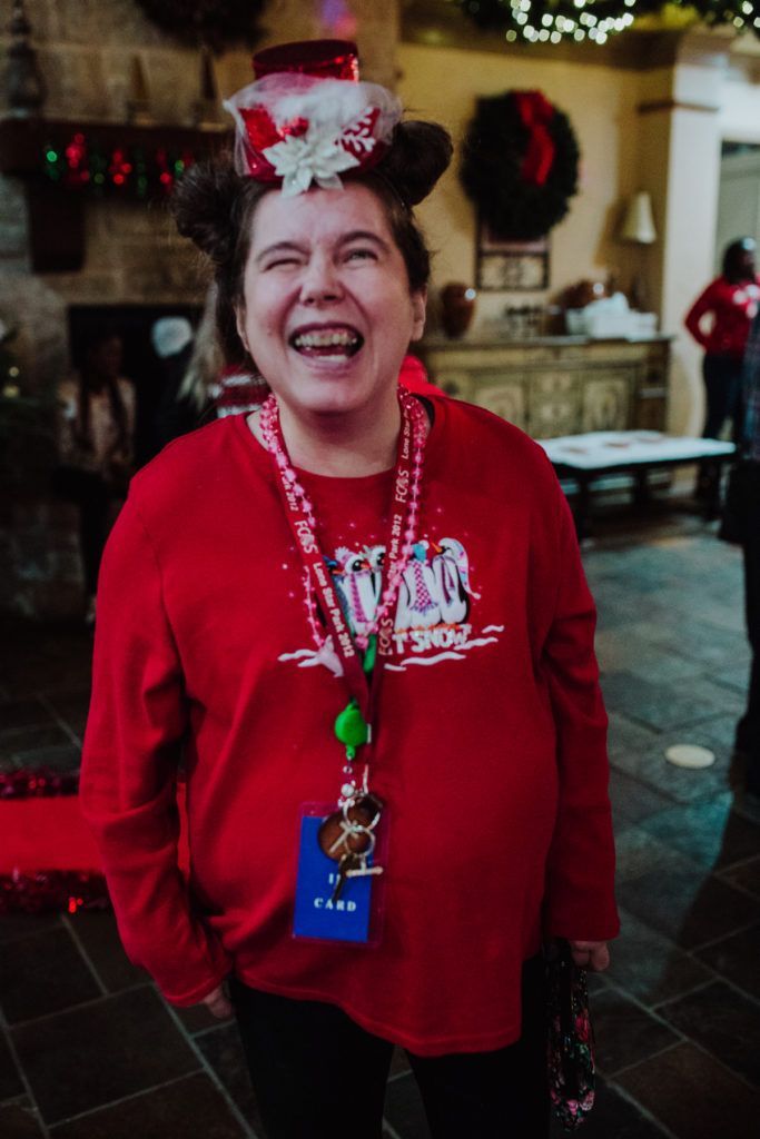A woman wearing a red shirt and a mickey mouse hat is laughing.