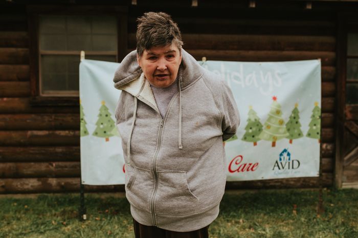 A woman in a hoodie is standing in front of a log cabin.
