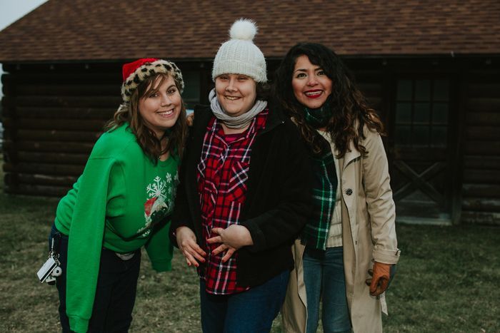 Three women are posing for a picture in front of a log cabin.
