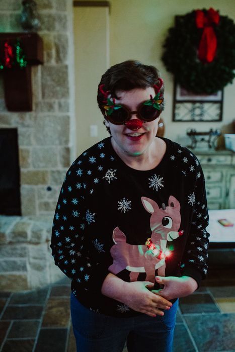 A man wearing a christmas sweater and sunglasses is standing in a living room.