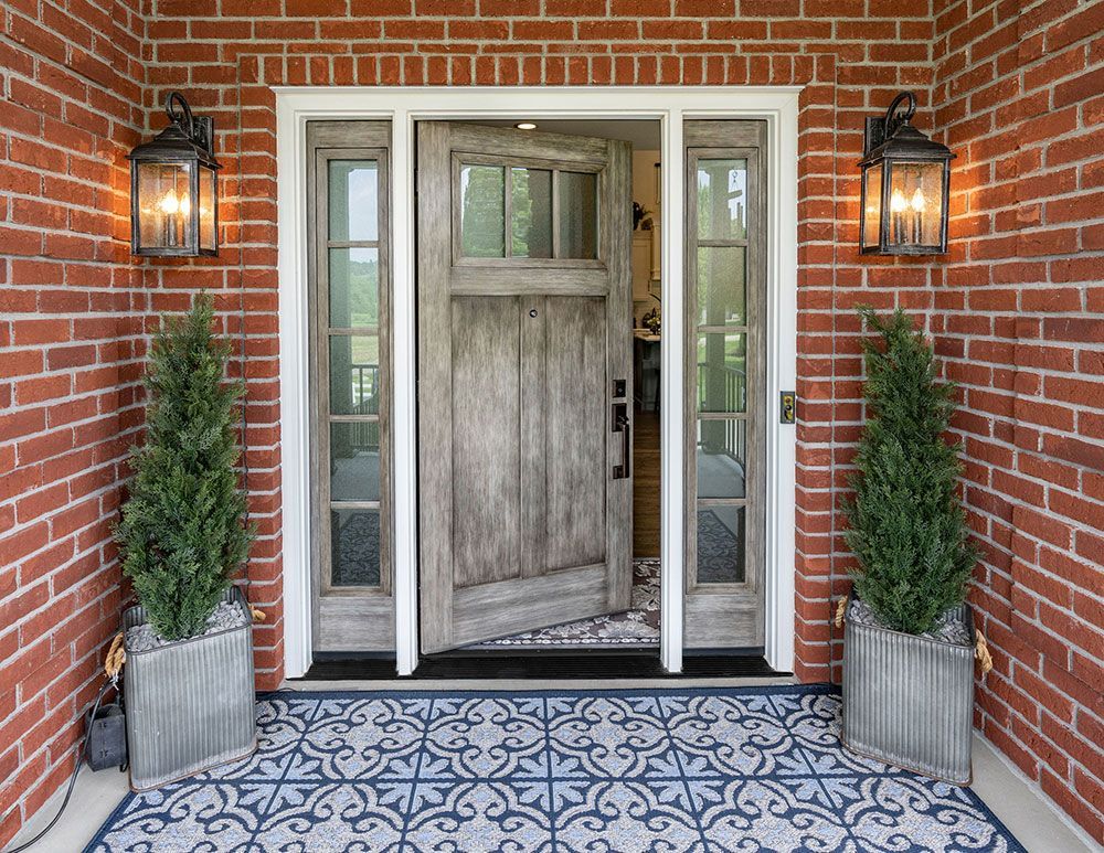 The front door of a brick house with a wooden door and a rug.