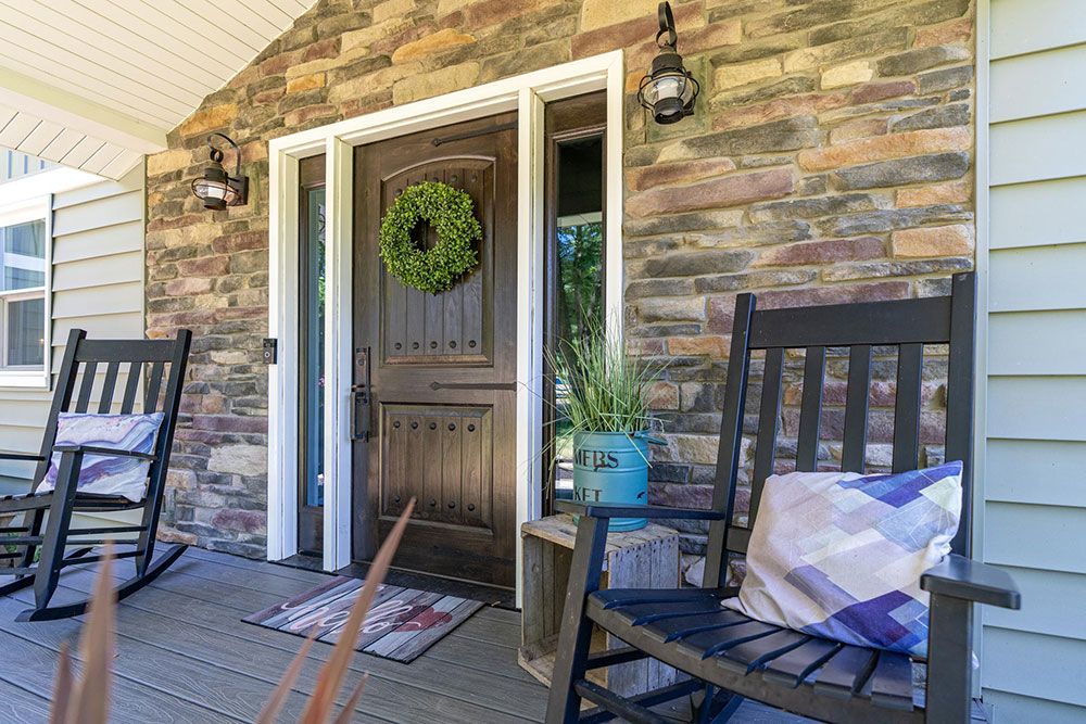 A porch with rocking chairs and a bench in front of a house.