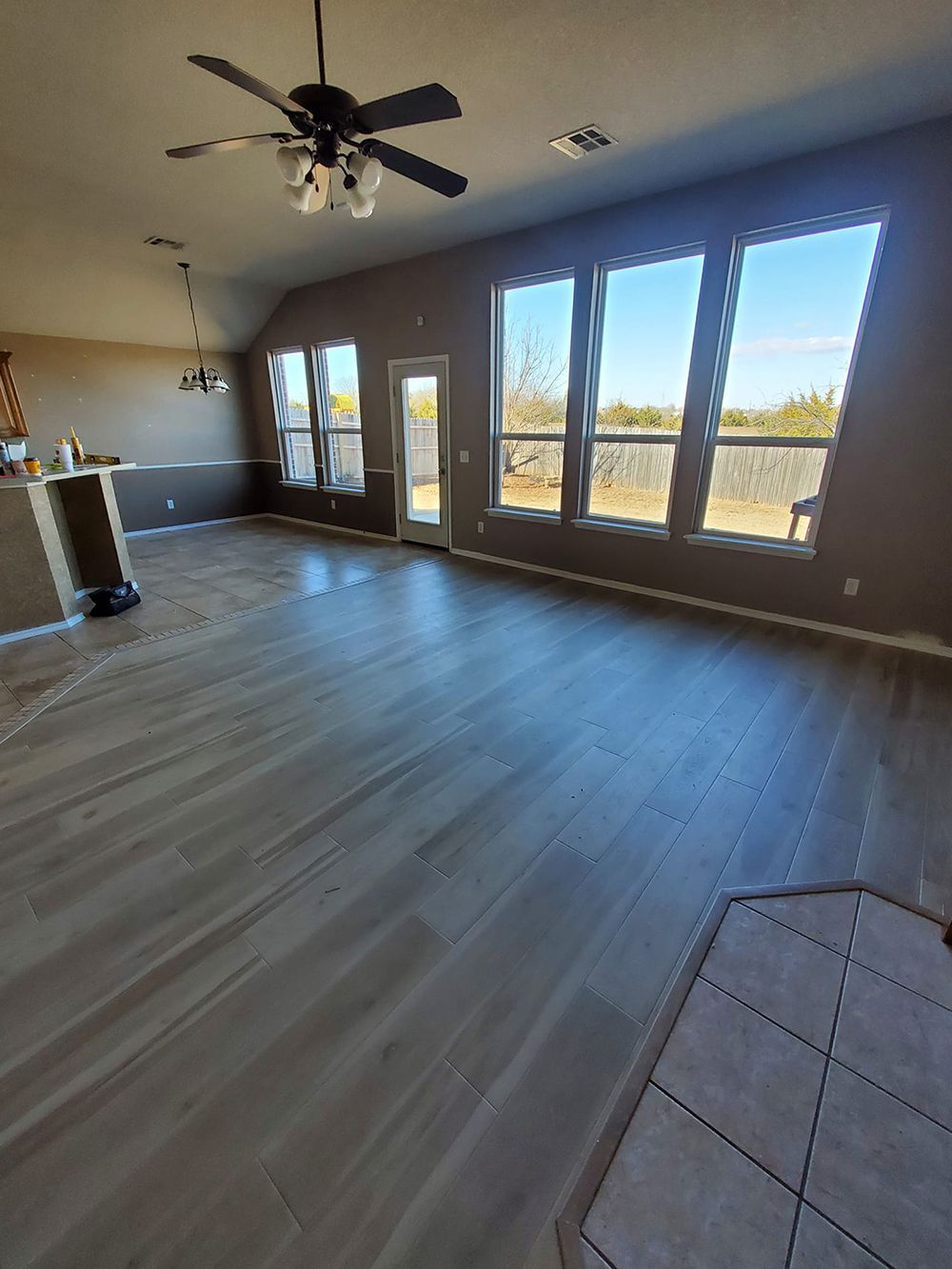 Living room with dark brown walls, light wood-look flooring, large windows, and a ceiling fan.