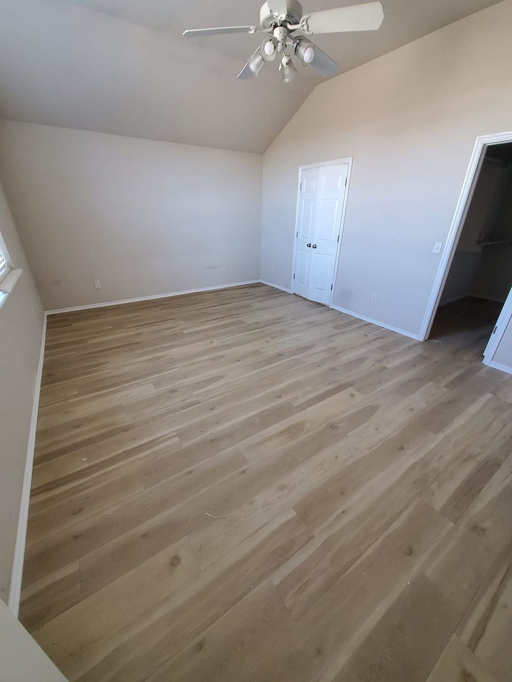 Empty bedroom with light wood-look flooring, a white door, and a ceiling fan.
