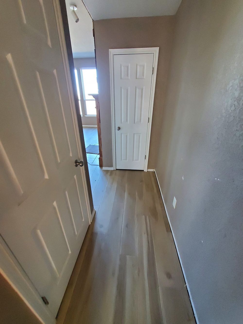 Narrow hallway with light wood floor, beige and gray walls, and two closed doors.