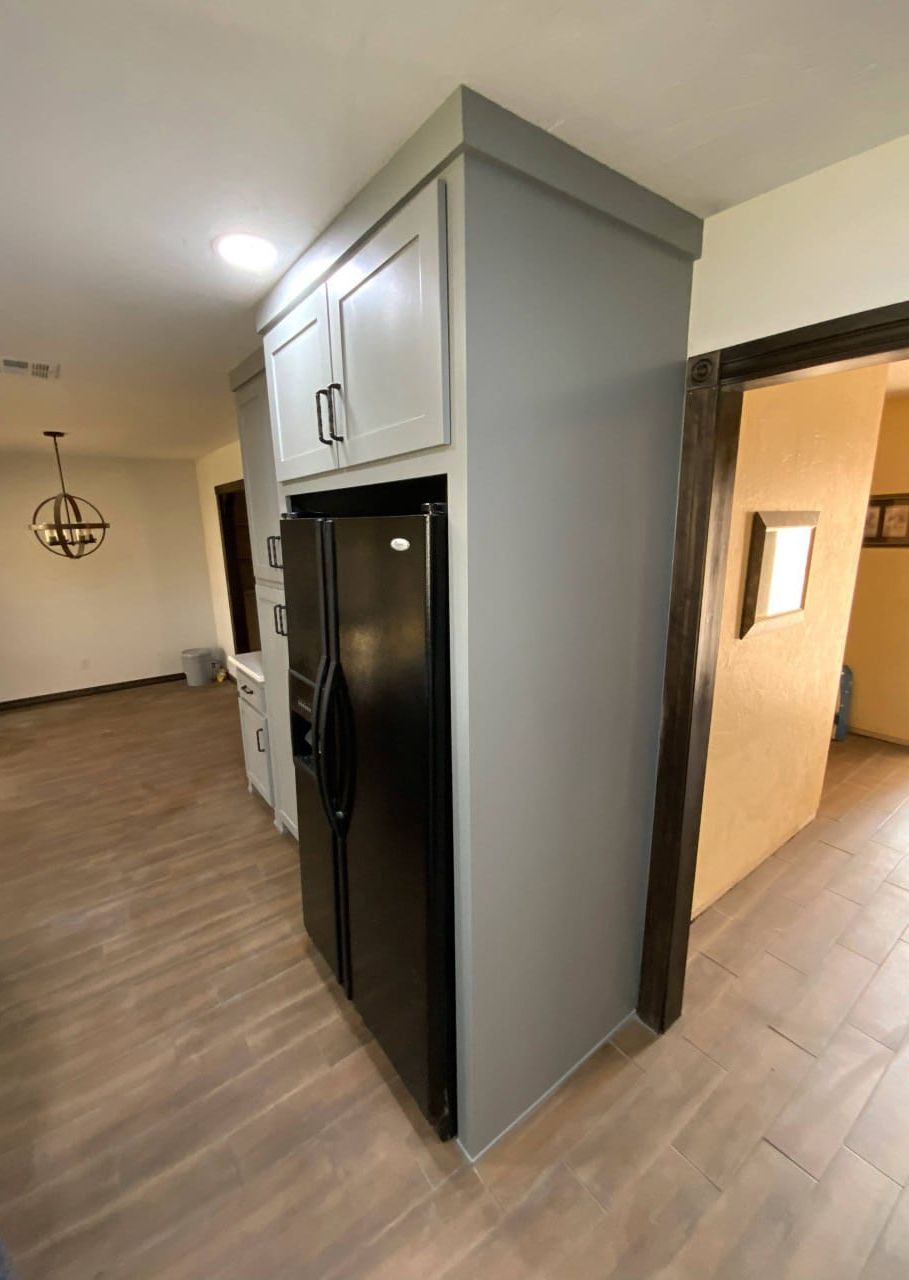 Tall grey cabinet with white upper cabinets and a black refrigerator.