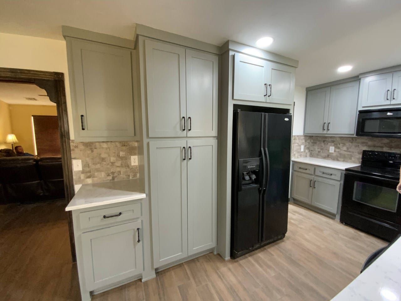 Kitchen with gray cabinets, black appliances, and light wood-look flooring.