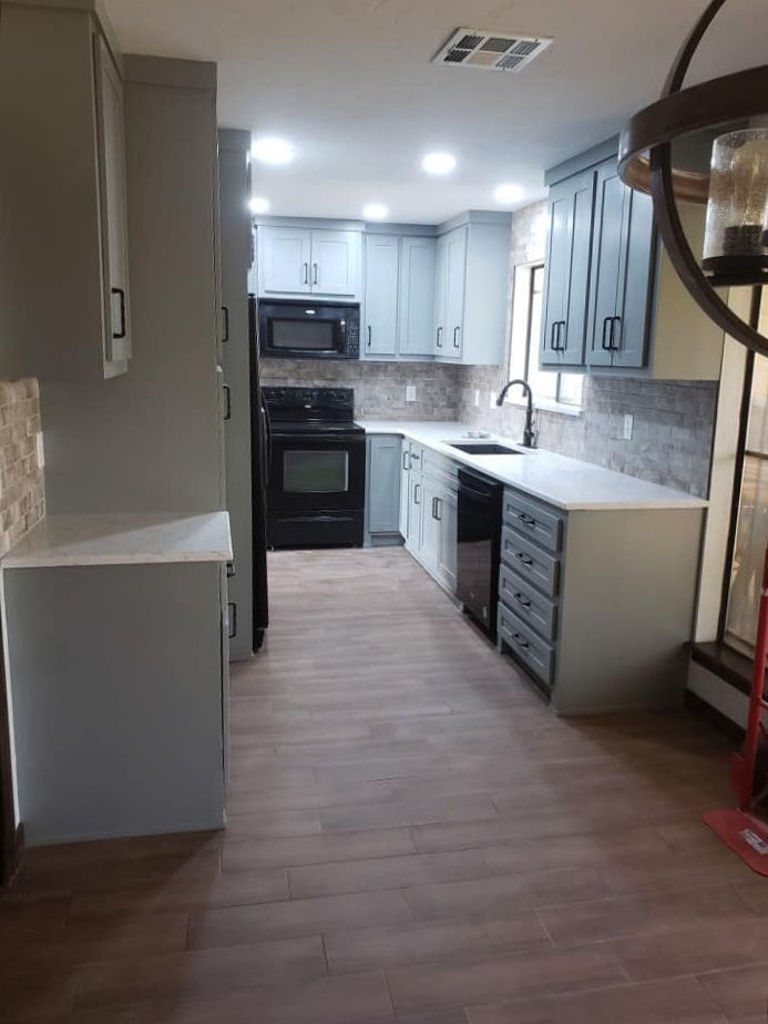 Modern kitchen with gray cabinets, black appliances, white countertops, and wood-look flooring.