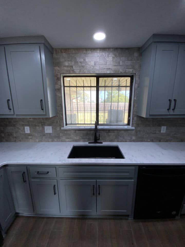 Light blue kitchen cabinets with black accents, a black sink, and a window with a backyard view.