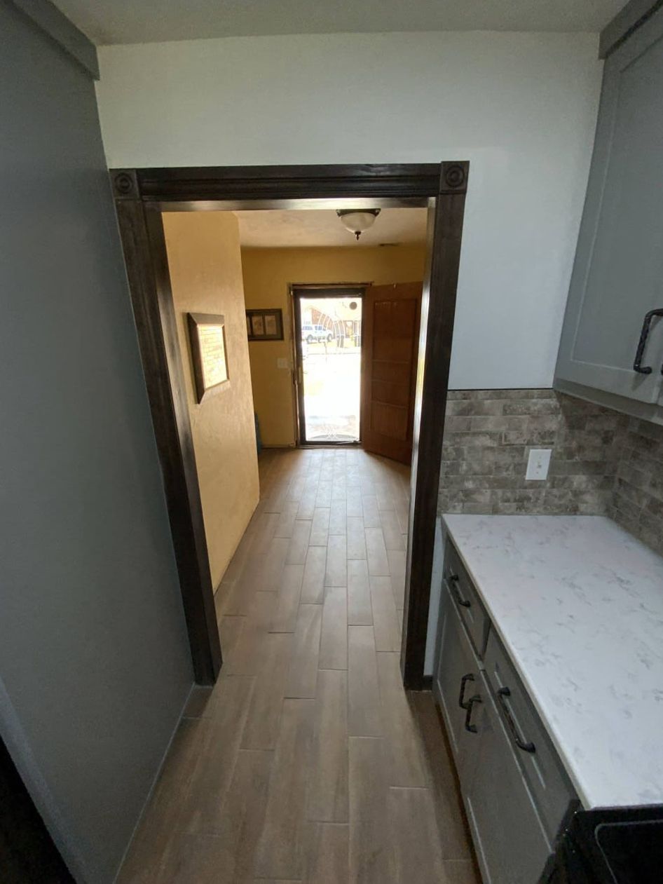 Narrow hallway with wood-look flooring, leading to an open door. Kitchen counter on right.