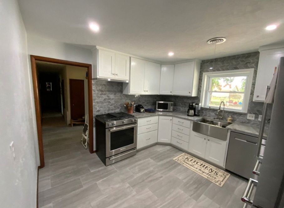 Modern white kitchen with stainless steel appliances and gray tile flooring.