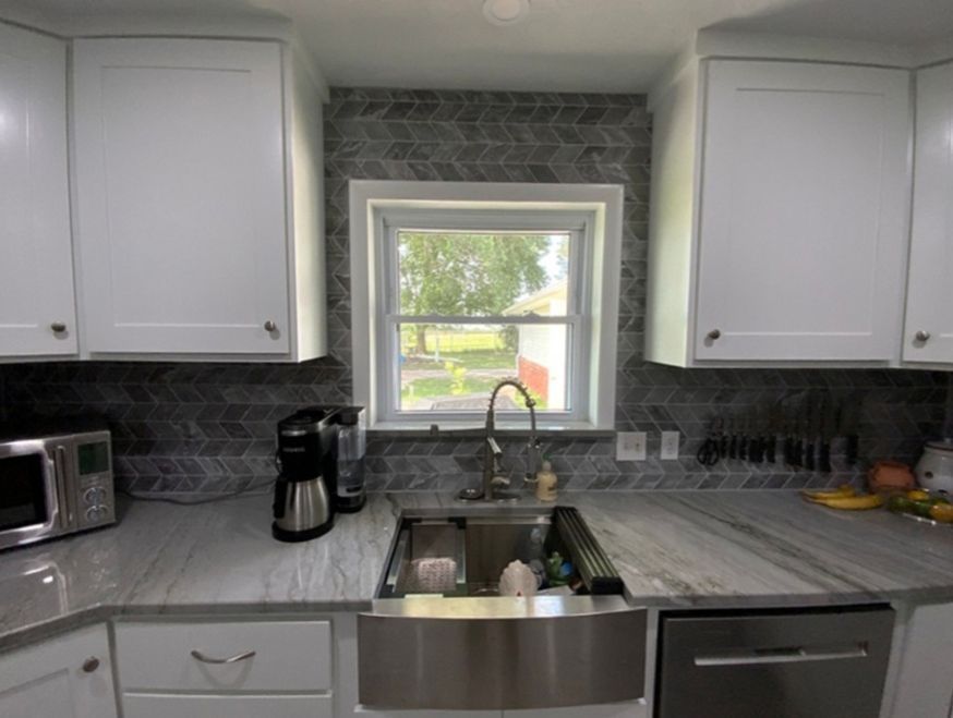 Kitchen with white cabinets, gray backsplash, stainless steel sink and appliances, and a window.
