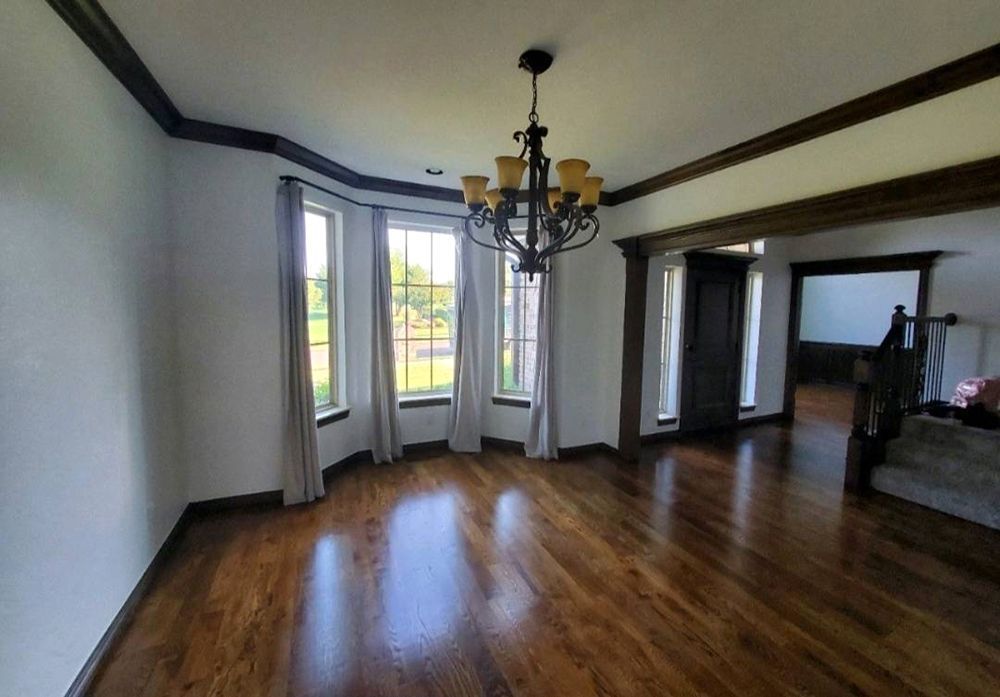 Dining room with hardwood floors, white walls, bay window, dark trim, and chandelier.