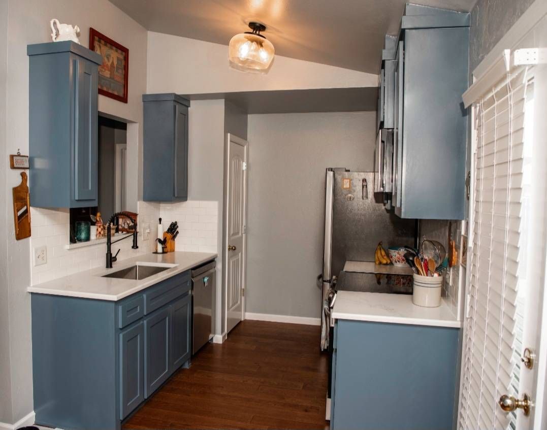 Blue kitchen cabinets and countertops with stainless steel appliances and dark wood flooring.