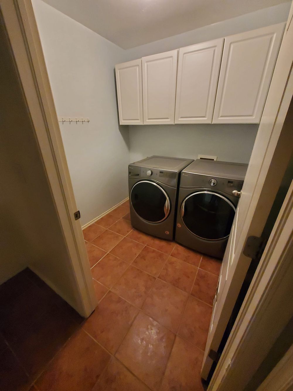 Laundry room with gray washer and dryer, tan tile floor, and white cabinets.