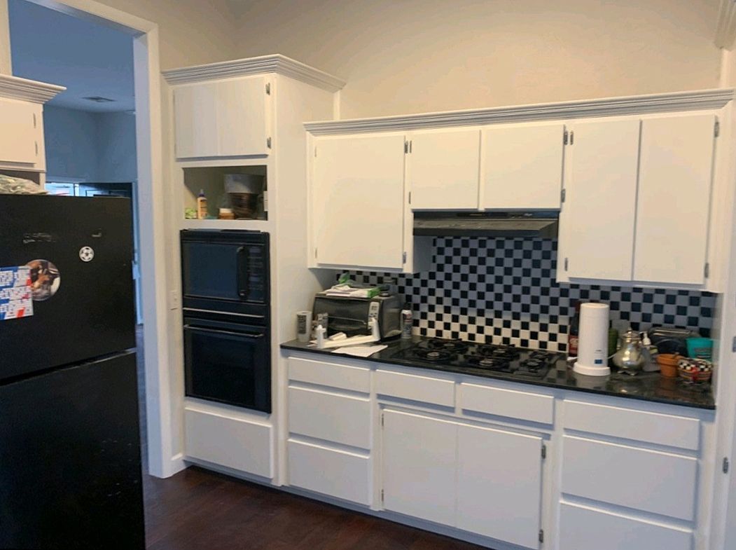 White kitchen with black appliances, dark countertops, and checkered backsplash.