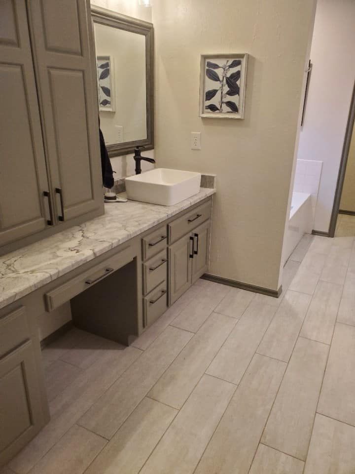Bathroom with gray cabinets, white sink, and marble countertop. Light wood-look flooring.