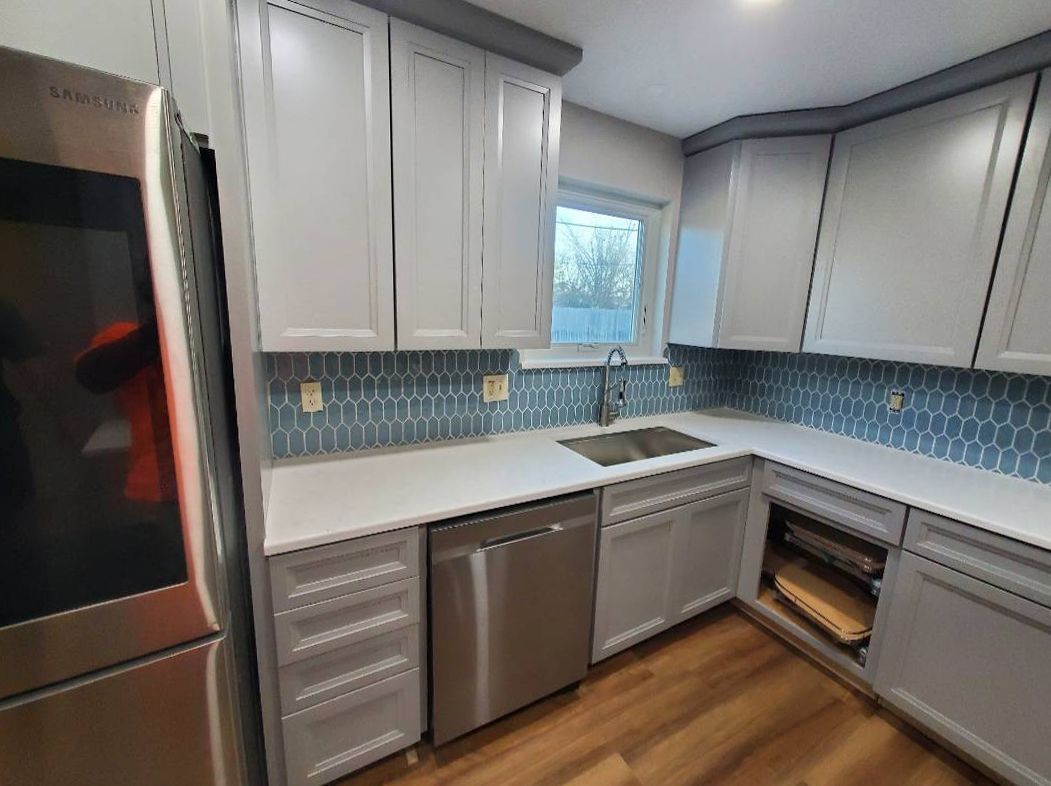 Gray and white kitchen with blue tile backsplash, stainless steel appliances, and light wooden floors.