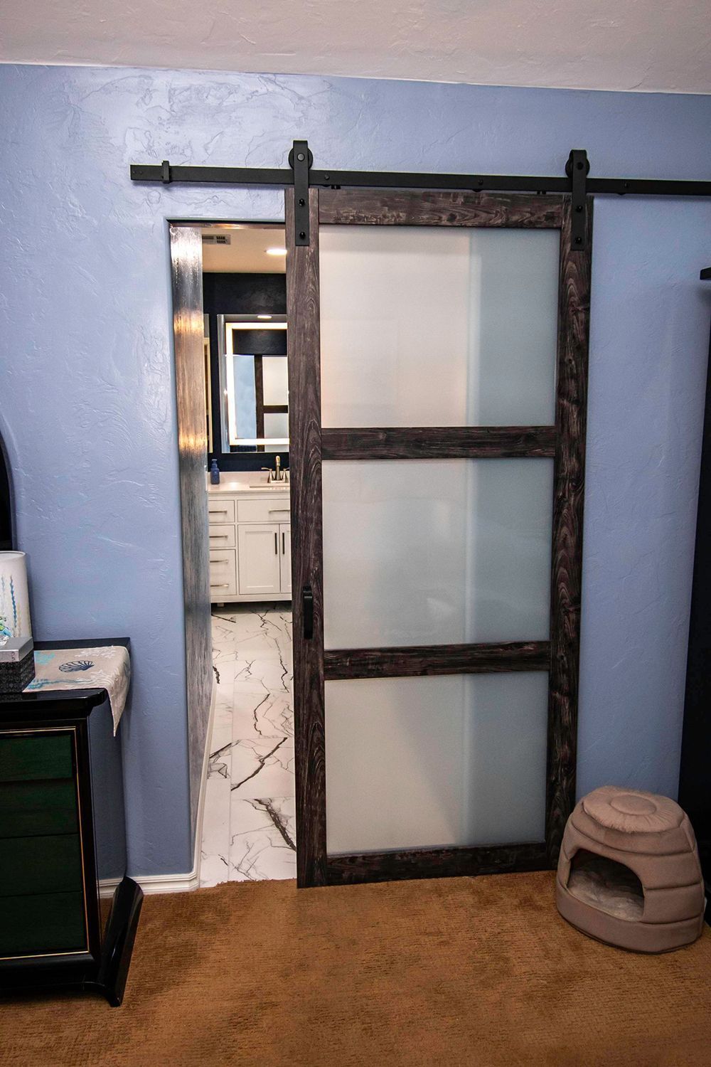 Barn door with frosted glass panels leads to a bathroom with a white vanity.