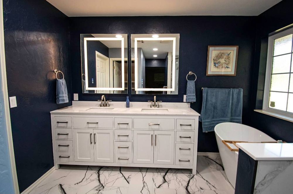 Blue bathroom with white vanity, lit mirrors, and soaking tub.