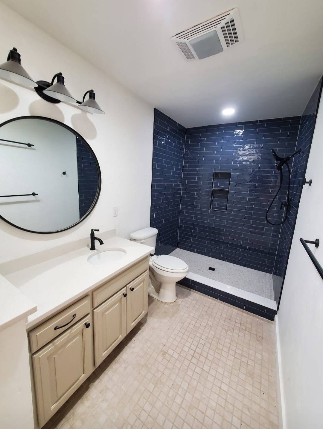 Modern bathroom with navy blue tiled shower, white vanity, and black fixtures.