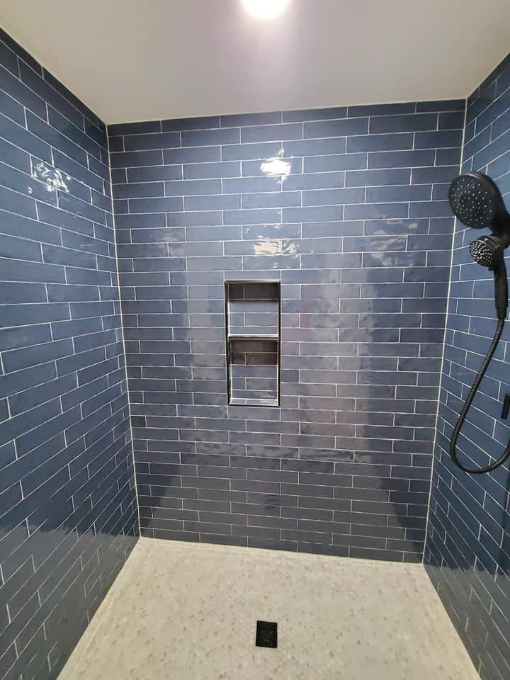 Blue tiled shower with recessed shelf and black shower head.