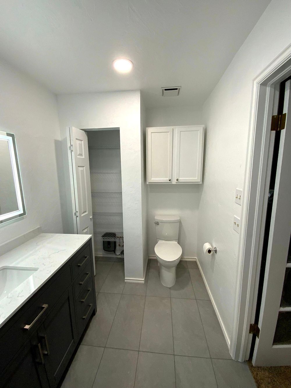Bathroom with dark vanity, white walls, gray floor, and toilet.