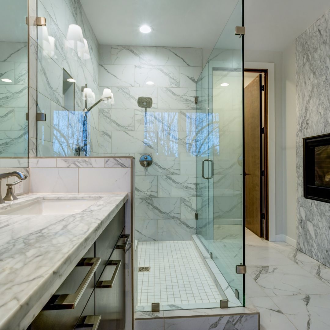 Bathroom with marble walls, glass shower, sink, and a fireplace.