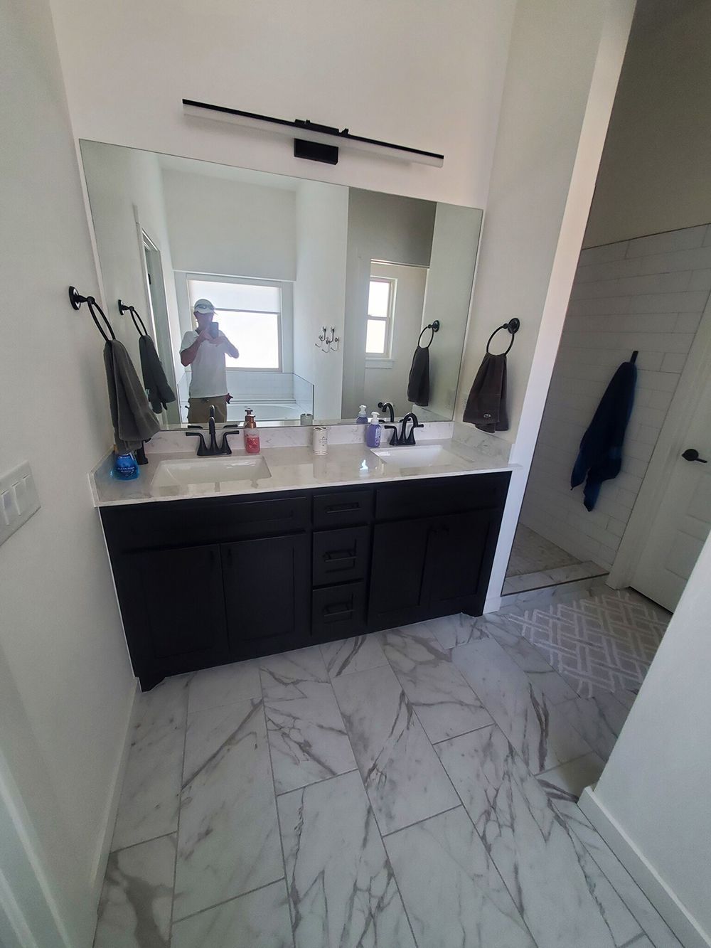 Bathroom with black double vanity, large mirror, and marble-patterned floor.