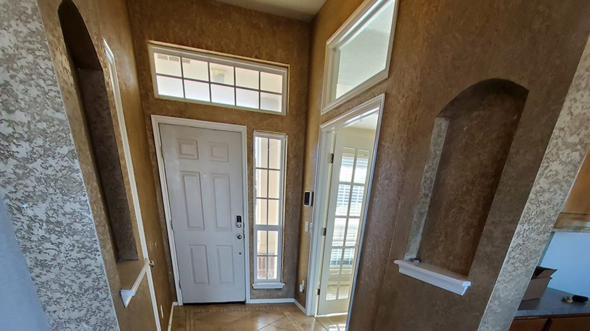 Entryway with beige textured walls, arched alcoves, white front door and windows.