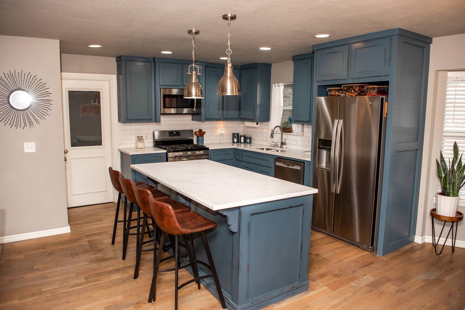 Blue kitchen with island and barstools, stainless steel appliances, white countertops, and a white door.