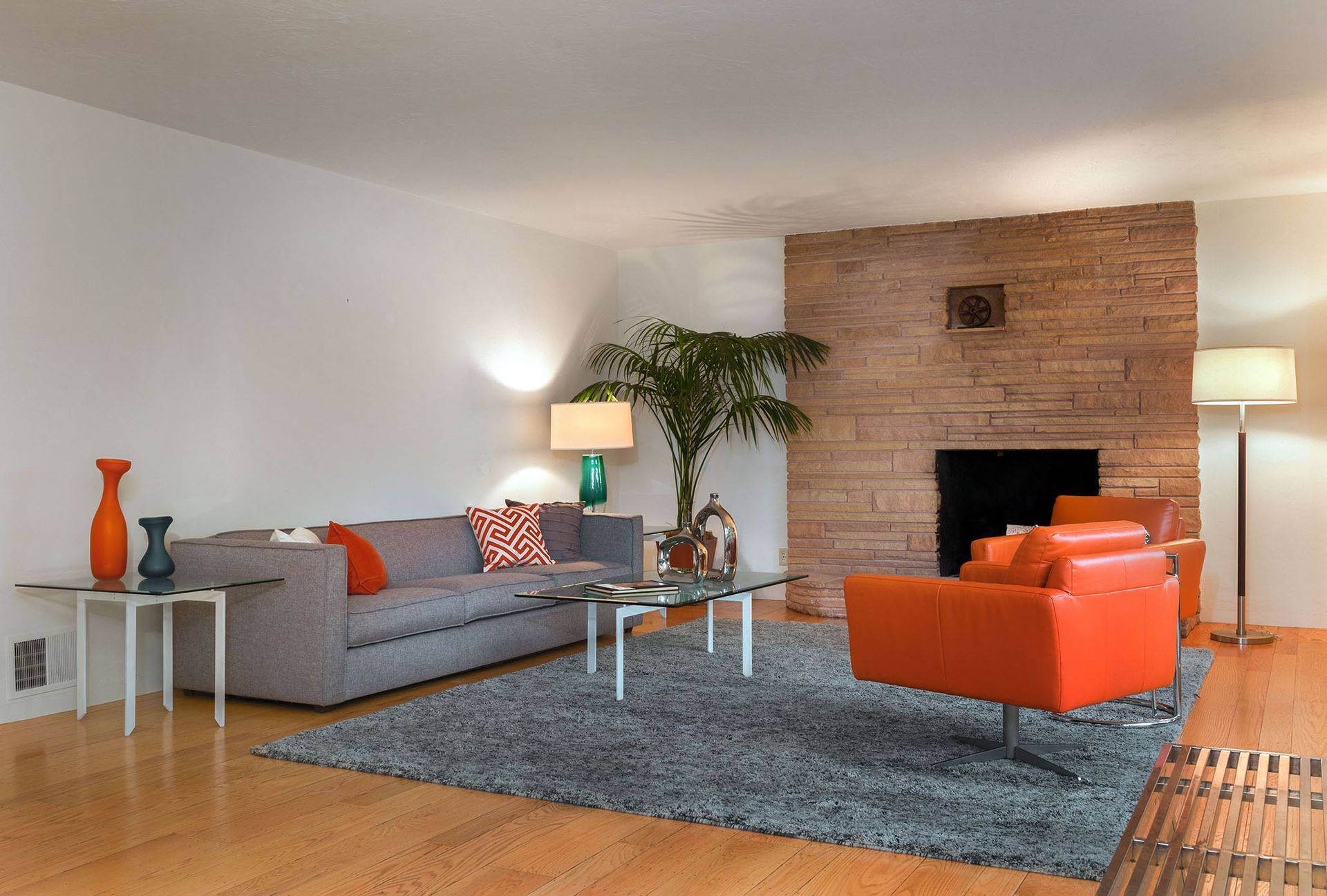 Living room with gray sofa, orange chair, and fireplace, on a gray rug.