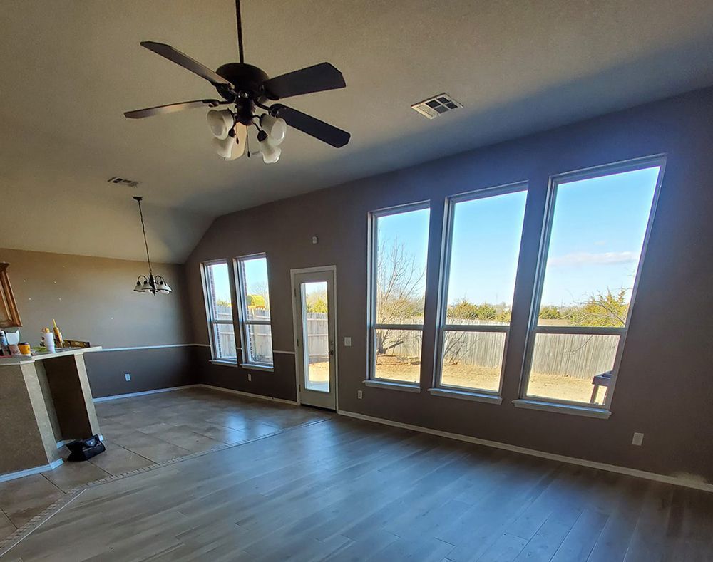 Living room with brown walls, large windows, ceiling fan, and wood-look floors.