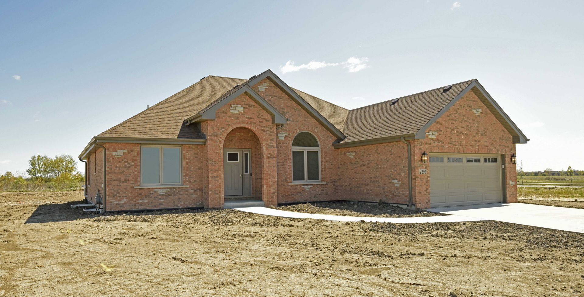 A brick house with a garage in the middle of a dirt field