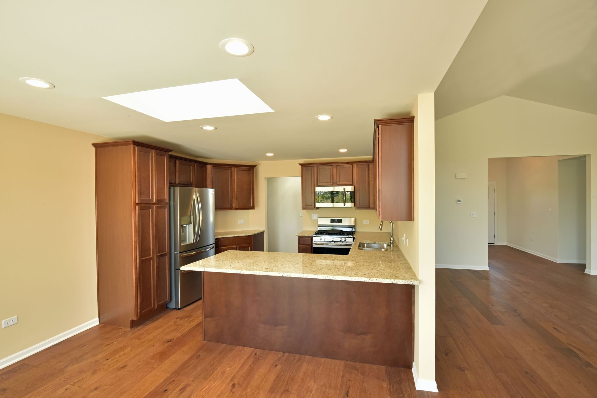 An empty kitchen with hardwood floors and stainless steel appliances