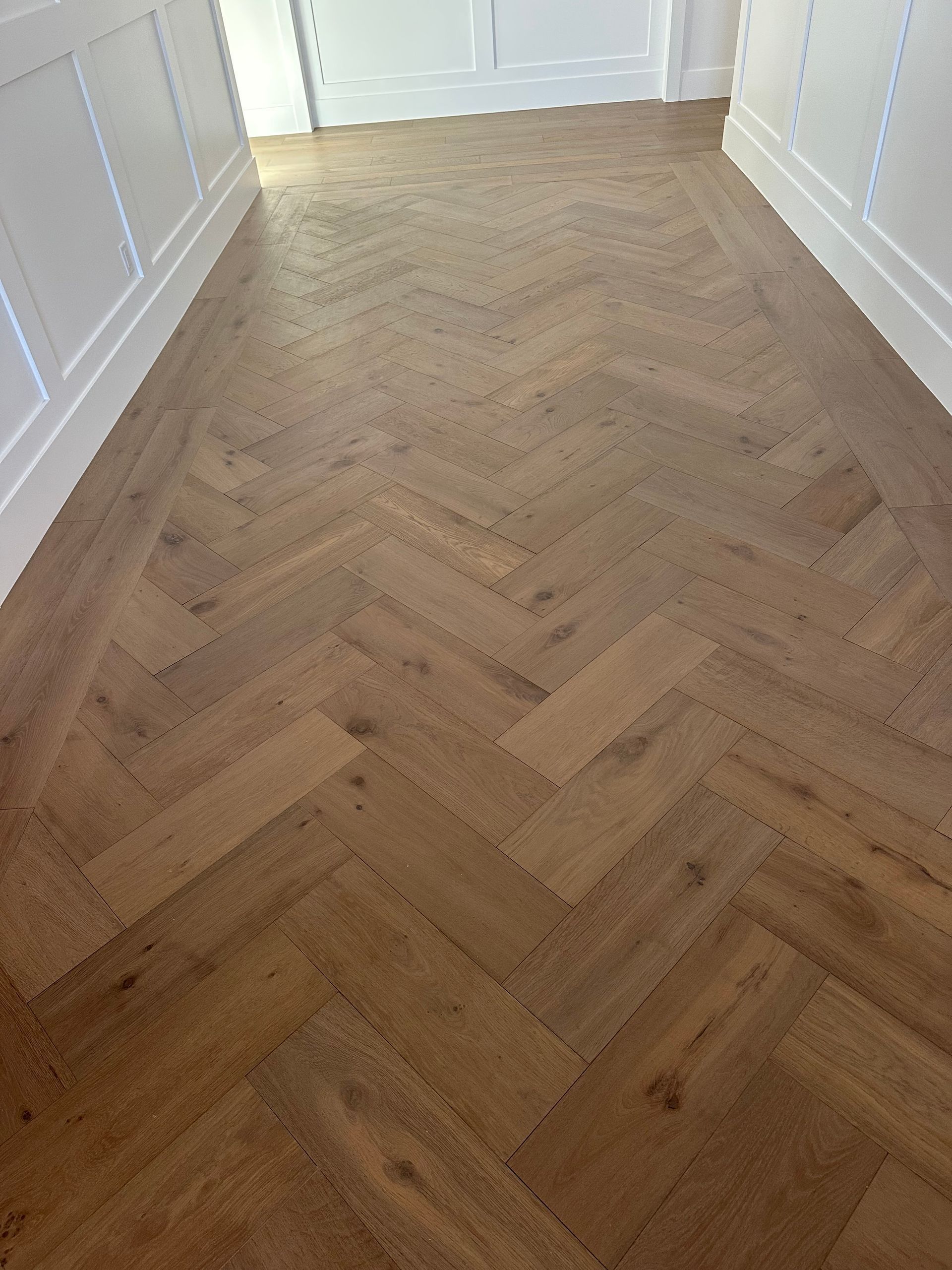 Empty hallway with herringbone wood floor and white walls